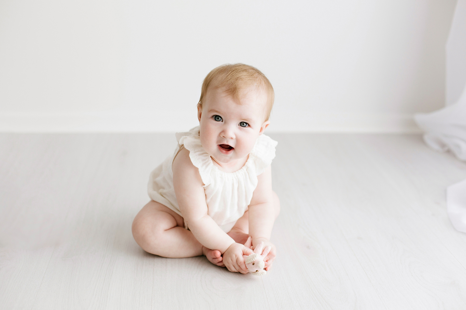 baby girl in a white romper sitting up and smiling