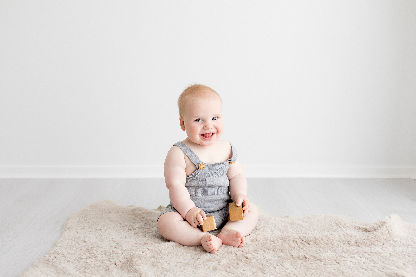 baby boy in grey overalls sitting and smiling