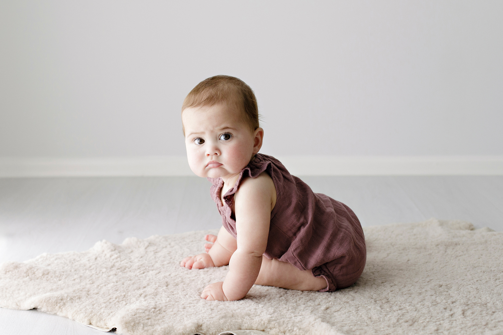 baby girl in a plum coloured romper looking very serious