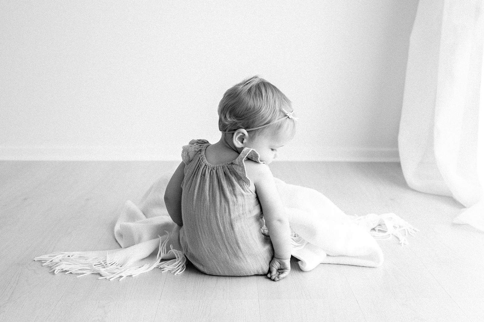 baby girl facing away from the camera looking down at her hand