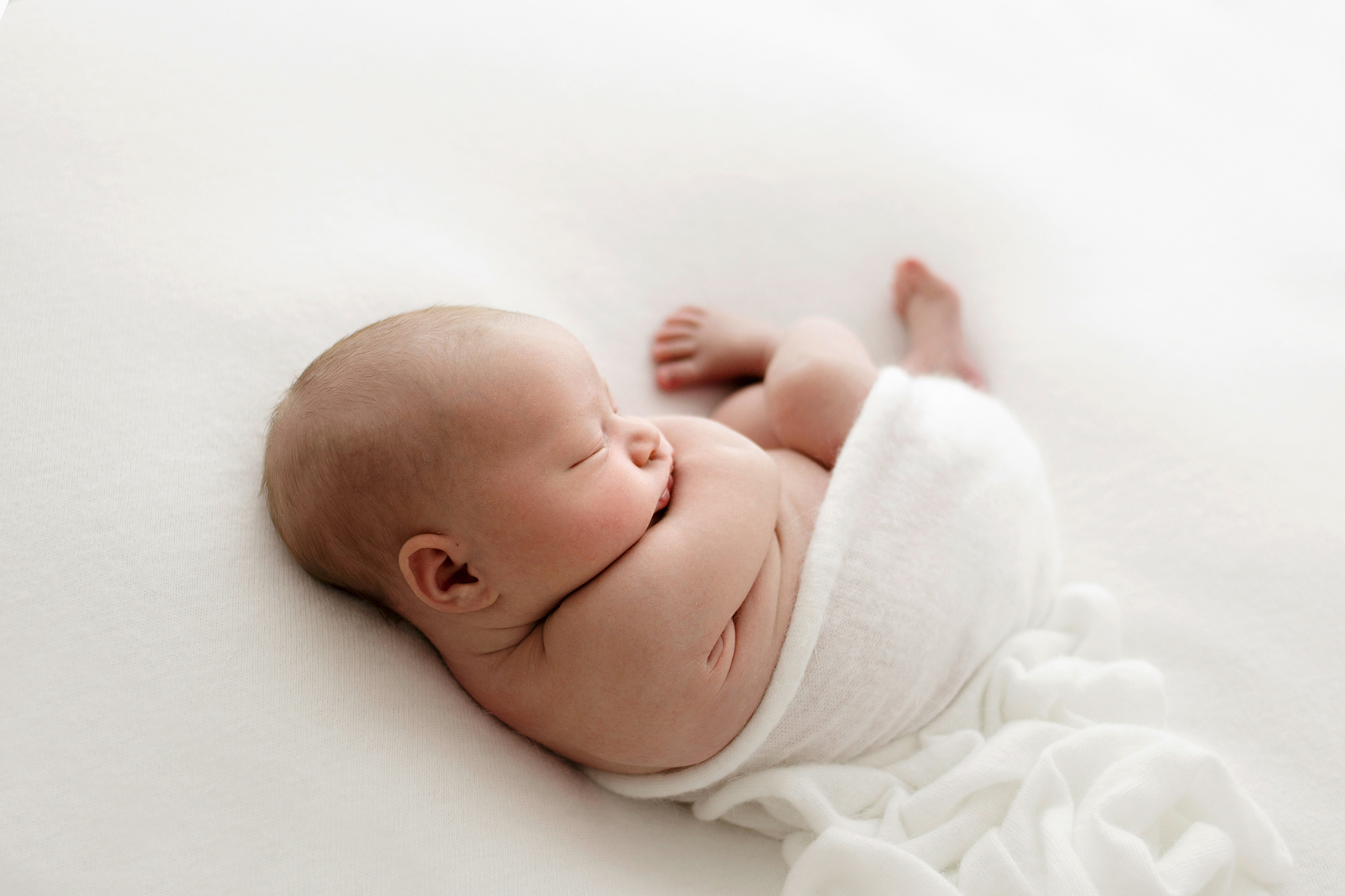 baby curled on a cream blanket